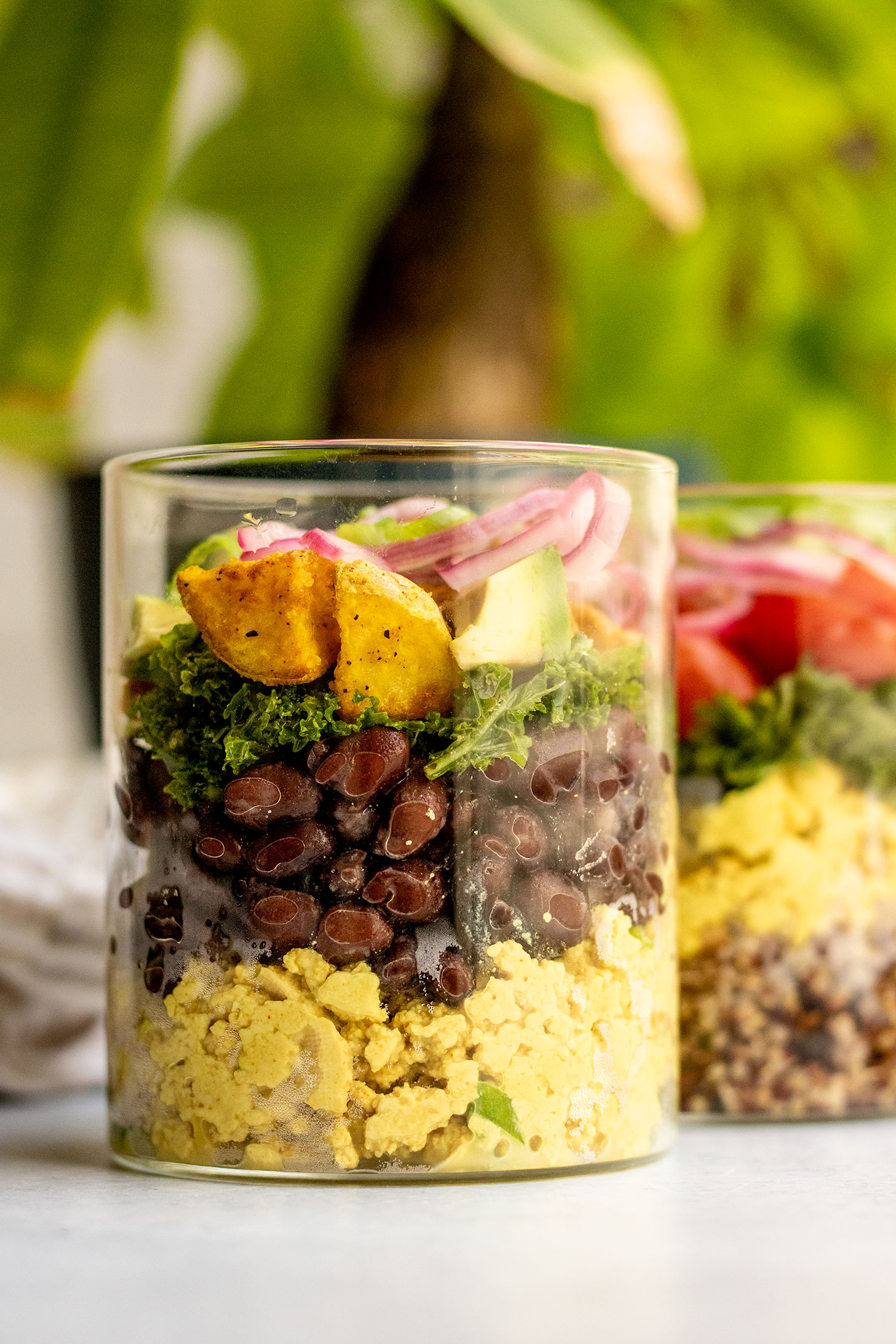 Close up of a jar filled with tofu scramble, black beans, potatoes, avocado, and pickled onions.