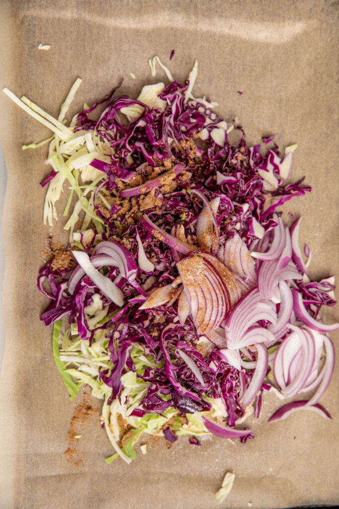 Seasoned red and green shredded cabbage, onions, and seasonings on a baking tray.