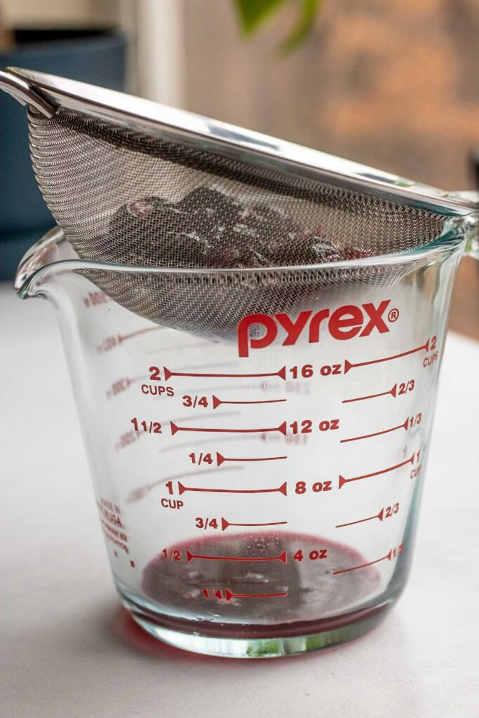 Mashed blueberries sitting over a strainer on top of a measuring cup to collect it's juice.