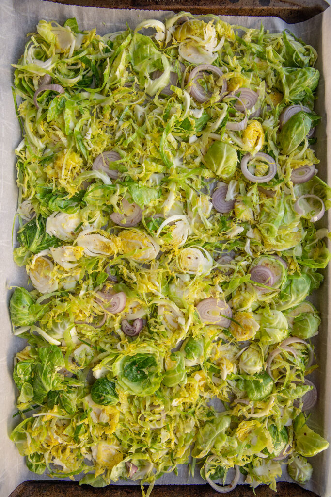 Seasoned brussels with shallots on a baking tray.