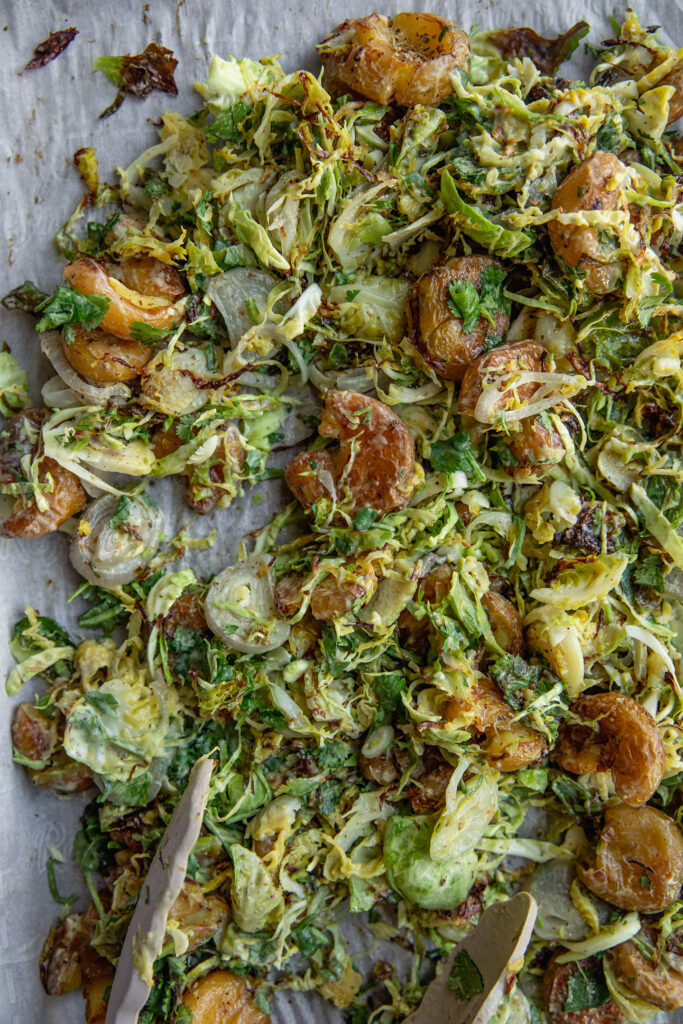 Mixing the avocado dressing with the brussels sprouts and baked potatoes on a tray.