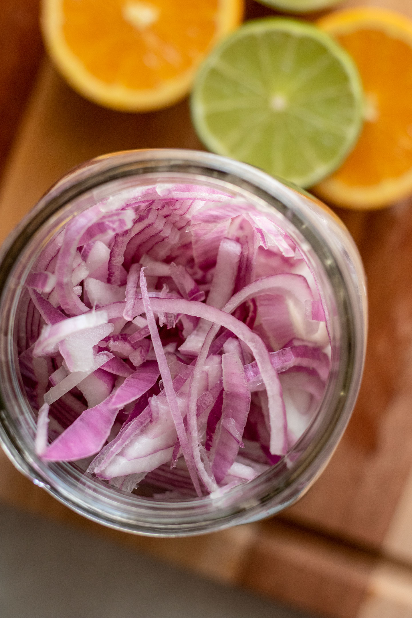 Sliced red onions stuffed into a jar with a few cut limes and oranges set around the base of the jar.
