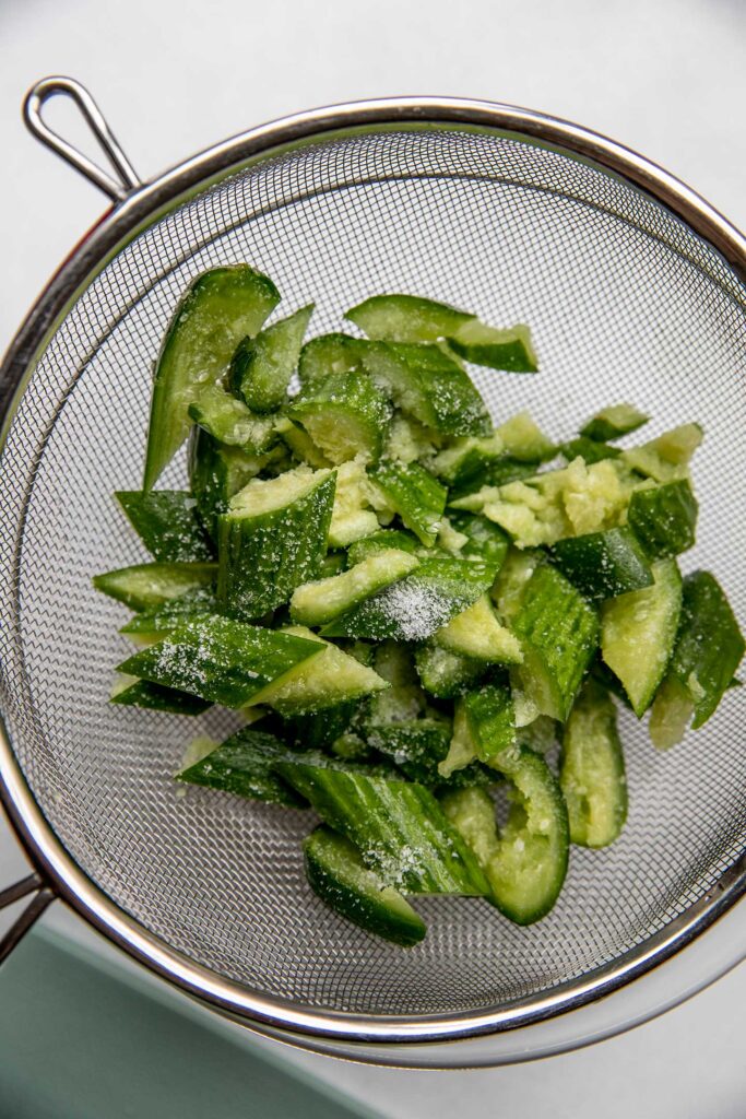 Smashed cucumbers in a mesh sieve.