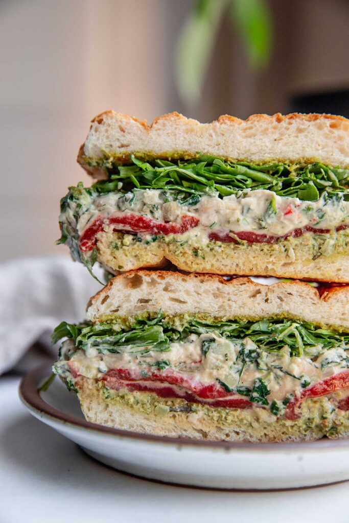 Close up of the filling of a sandwich stuffed with arugula, spinach artichoke white bean dip and red bell pepper.