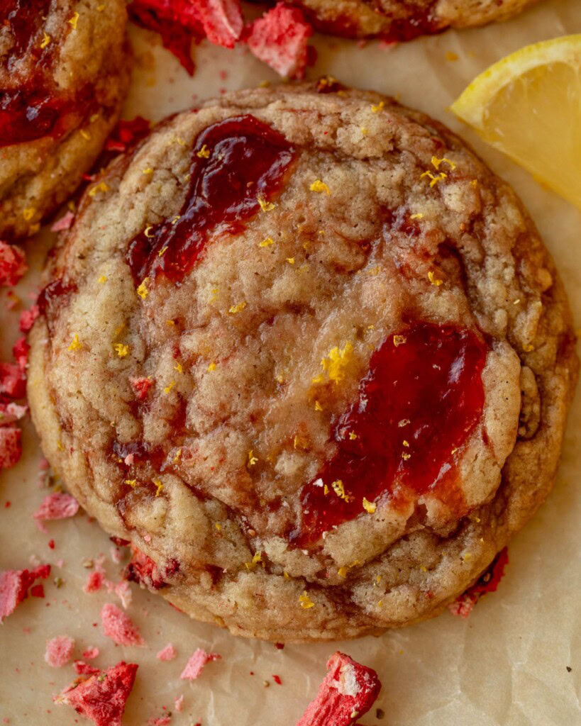 Close up of a cookie with pools of strawberry jam on top.