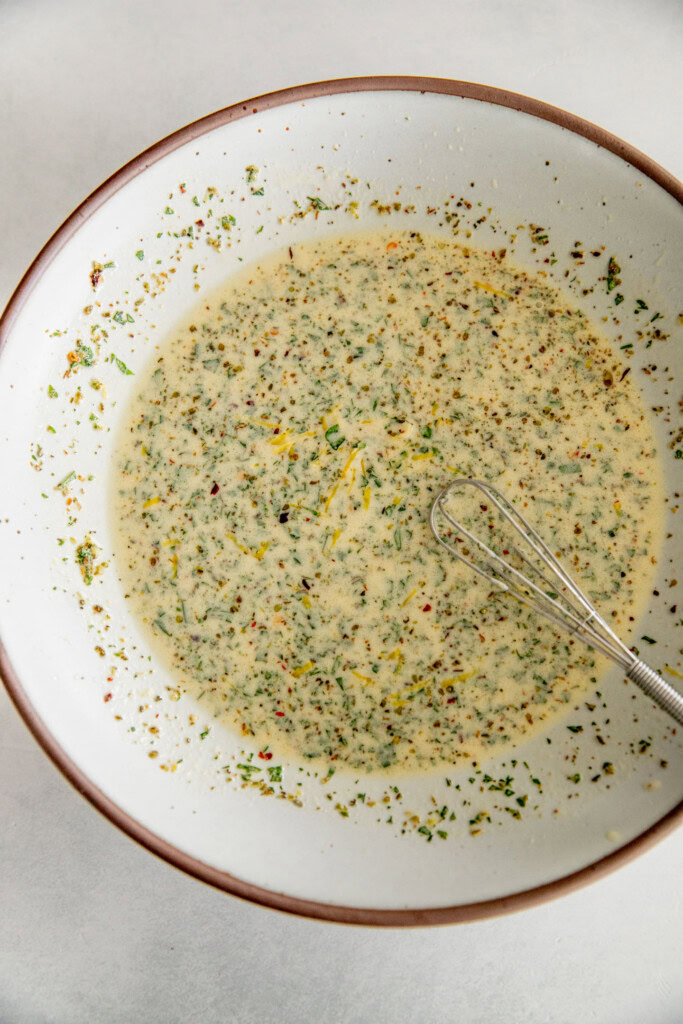 Mixing together the dressing with a tiny whisk in a large bowl.