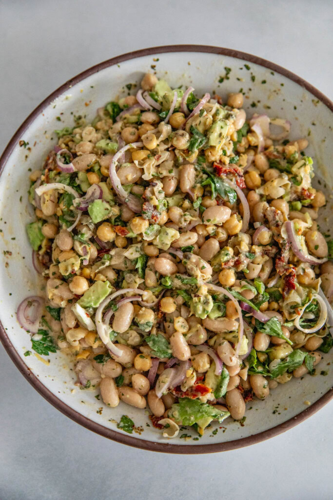 White bowl filled with mixed sun-dried tomato bean salad being stirred together with a spoon.