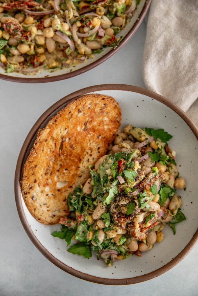 Top down shot of a small bowl of mixed bean salad served with a golden toasted piece of sourdough bread.