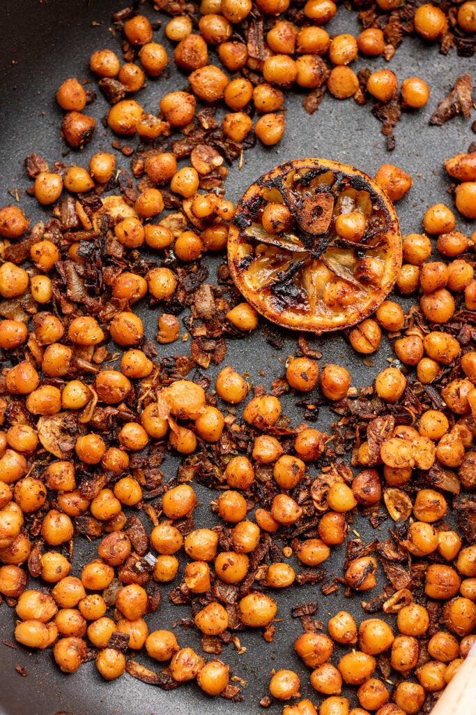 Seared and blistered chickpeas coated in spices in a pan.