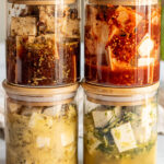 Four jars stacked on top of each other filled with 4 different marinades including balsamic tofu, gochujang tofu, tofu feta and cilantro lime tofu.
