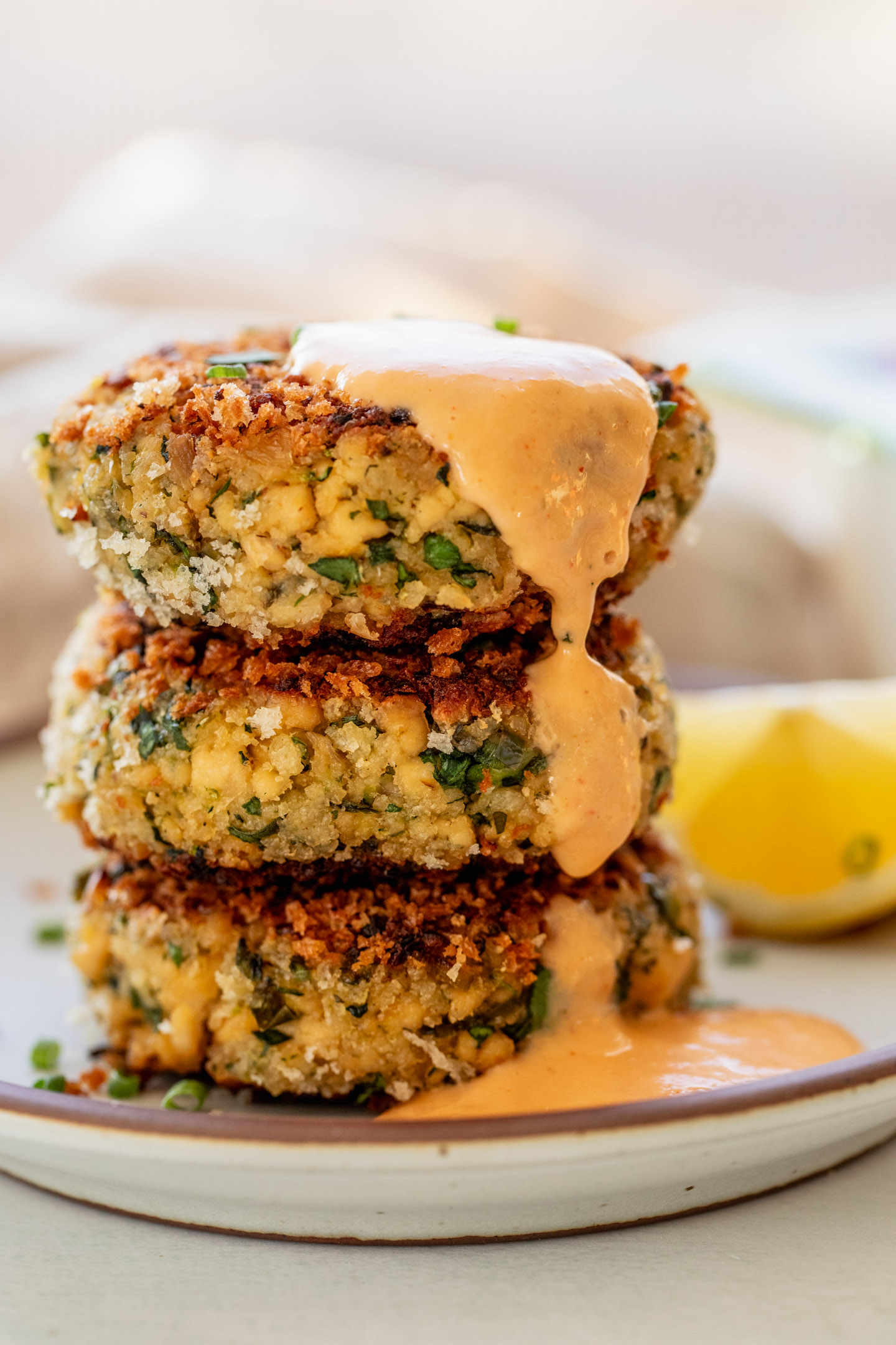 A stack of three tofu patties on a plate with kimchi mayo drizzled on top.