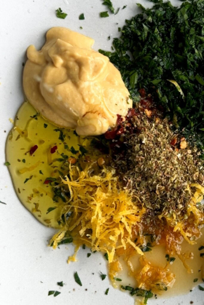 Bowl filled with mustard, mayo, sweetener, parsley, oregano, red pepper, lemon, and oil.