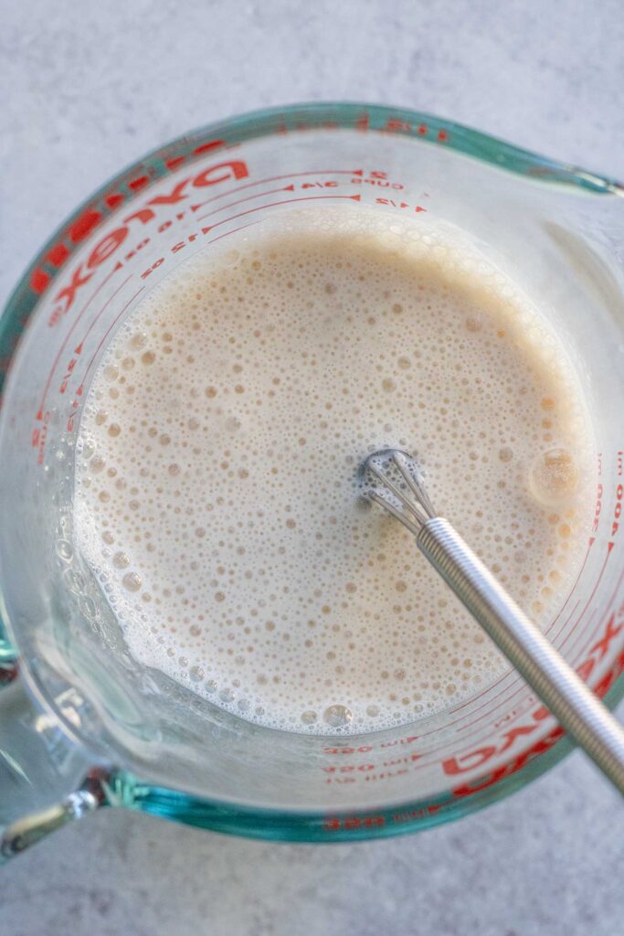 Whisking soy milk with apple cider vinegar in a large measuring cup.
