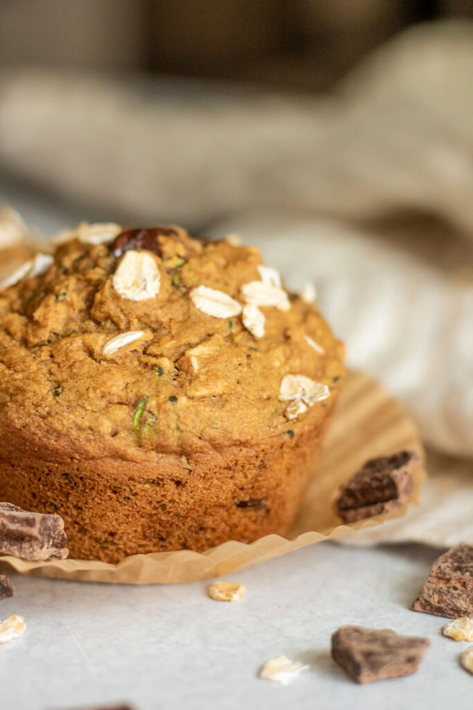 Close up of a chocolate chip zucchini muffin on top of a pulled away wrapper. 