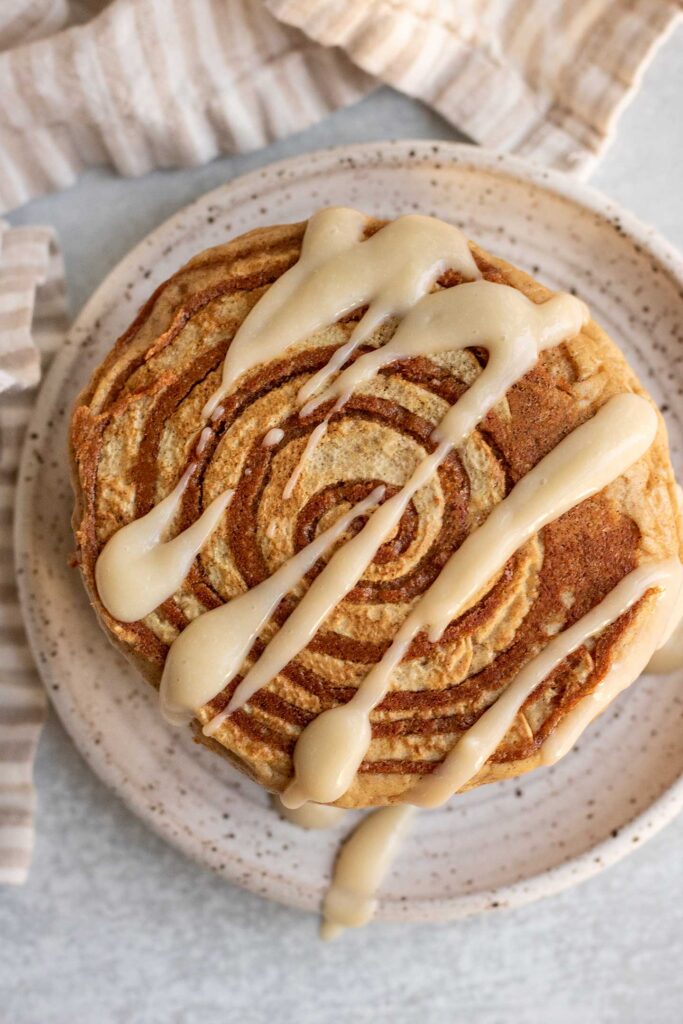 Top down view of a stack of pancakes showing off the cinnamon sugar swirl on top with a drizzle of maple cream cheese glaze.