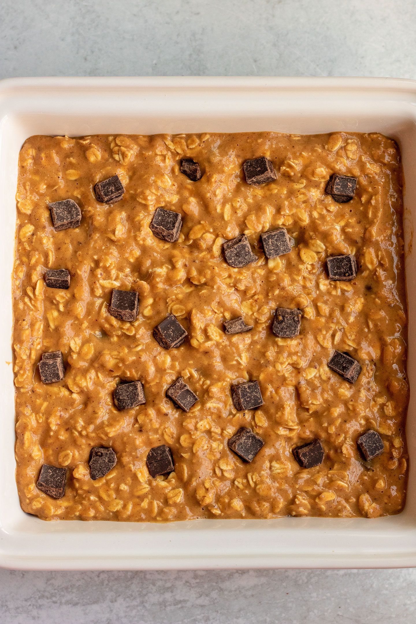 Pumpkin oat batter spread in a baking dish with chocolate chips placed on top.