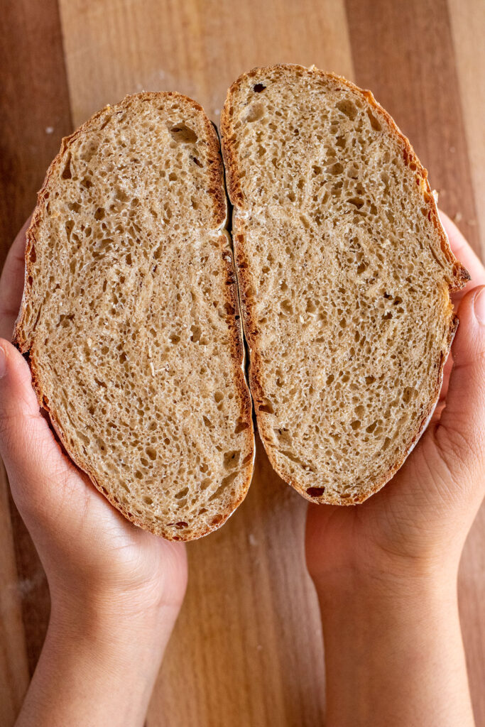 The bread cut in half and held in both hands to showcase the inside of the cooked bread.
