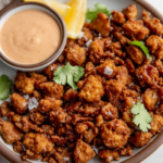 Plate of crispy baked tofu pieces served with a side bowl of yogurt sauce and lemon wedges.