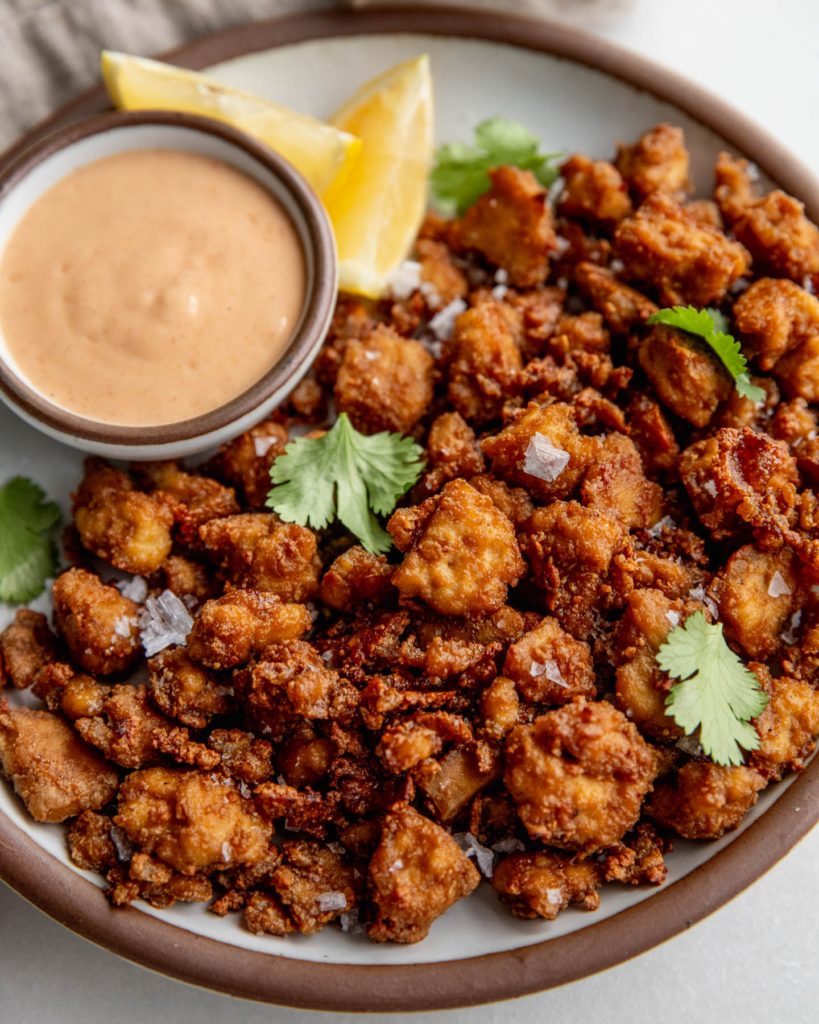 Plate of crispy baked tofu pieces served with a side bowl of yogurt sauce and lemon wedges.