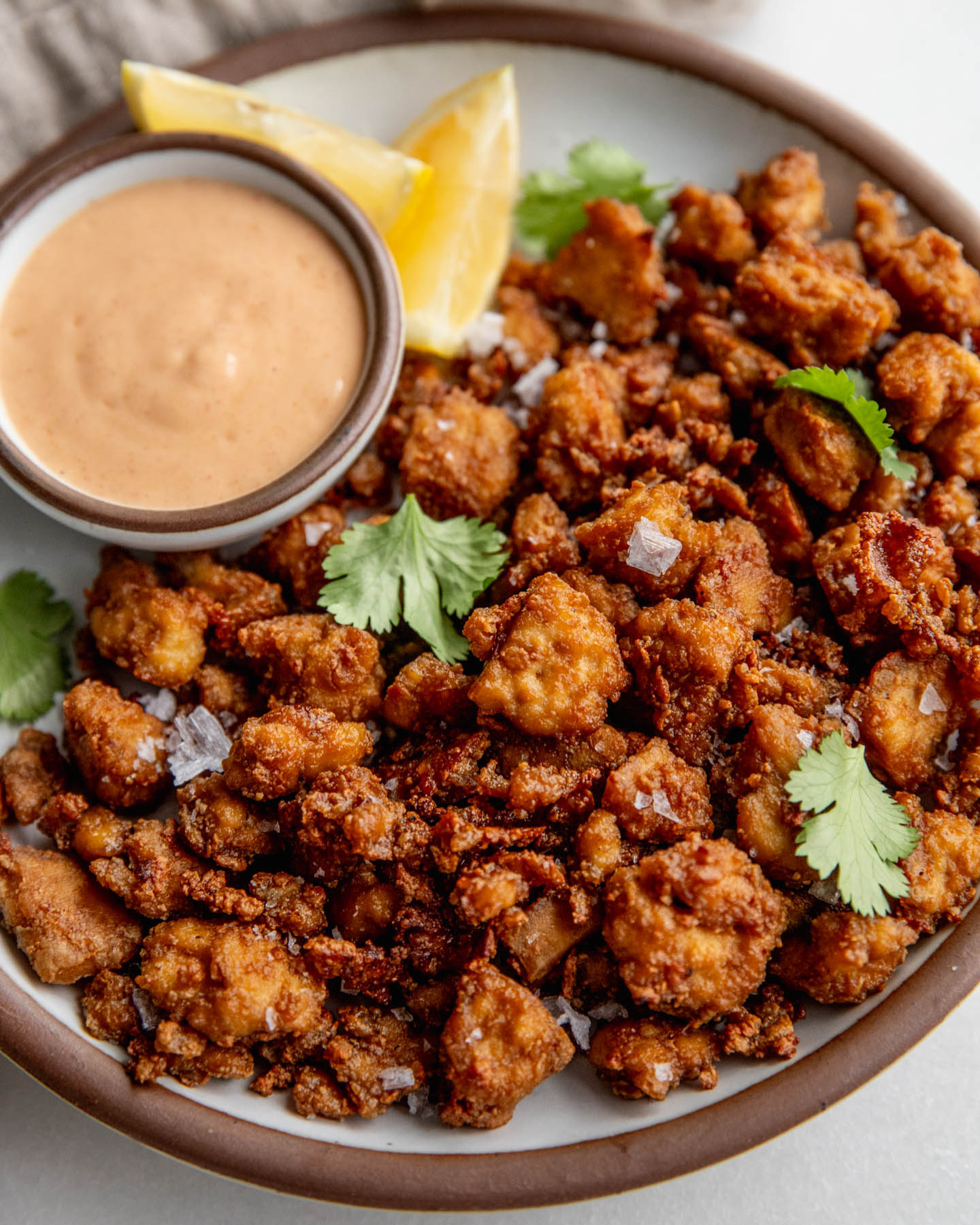 Plate of crispy baked tofu pieces served with a side bowl of yogurt sauce and lemon wedges.